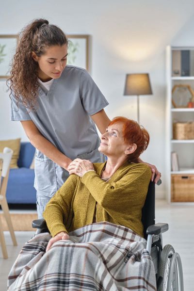 Pflegefachkraft kümmert sich um eine ältere im Rollstuhl sitzende Frau im häuslichen Umfeld